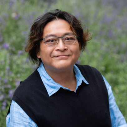 Headshot of Eric Tang with a slight smile on his face. He's wearing silver framed glasses